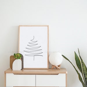 May include: A framed black and white line drawing of a stylized Christmas tree on a white background. The frame is made of light wood. The drawing is on a wooden shelf with a white ceramic vase with a small green plant, a wooden decorative object, and a white moon lamp on a wooden stand. The shelf is part of a white cabinet with two drawers. The cabinet has a wooden top and wooden drawer pulls. A green snake plant is in a white pot on the right side of the image.