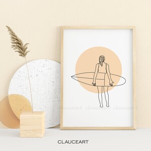 Pu&ograve; includere: Un disegno a linea di una persona che tiene una tavola da surf davanti a un cerchio color pesca. Il disegno &egrave; in bianco e nero ed &egrave; incorniciato in una cornice di legno chiaro.