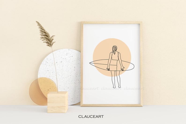 Pu&ograve; includere: Un disegno a linea di una persona che tiene una tavola da surf davanti a un cerchio color pesca. Il disegno &egrave; in bianco e nero ed &egrave; incorniciato in una cornice di legno chiaro.