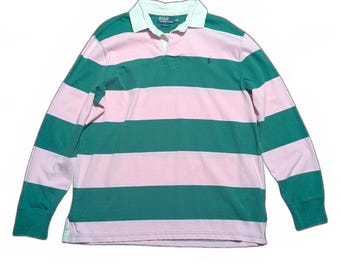 Puede incluir: Una camiseta de rugby de manga larga con rayas horizontales rosas y verdes. La camiseta tiene un cuello blanco y un pequeño logotipo bordado en el pecho. La camiseta está hecha de un material suave y cómodo.