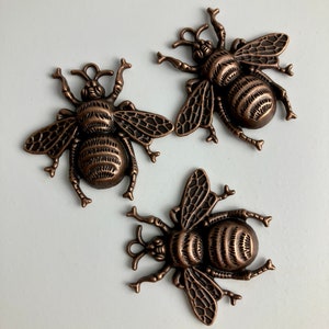 Pode incluir: Três pingentes de abelha de bronze antigo com detalhes intrincados. Cada pingente apresenta uma abelha detalhada com asas e um corpo texturizado.