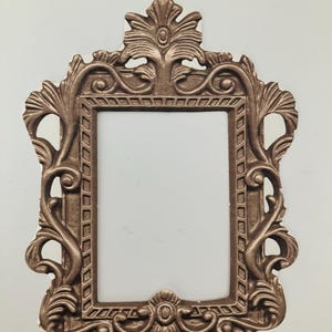 May include: An ornate gold picture frame with a detailed floral design. The frame is made of metal and has a rectangular shape.