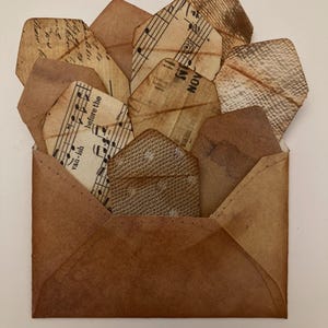 Puede incluir: Un sobre de papel marrón con varias etiquetas de papel pequeñas y envejecidas en su interior. Las etiquetas tienen notas musicales y texto impreso. El sobre y las etiquetas tienen una estética vintage y antigua.