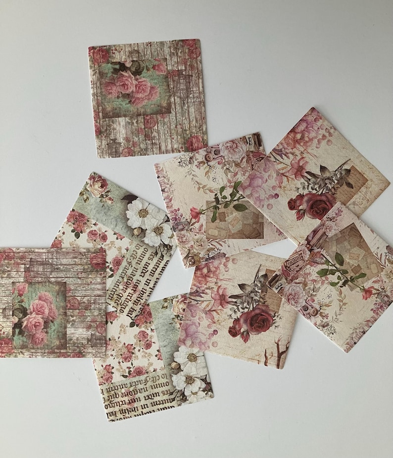 May include: A set of eight vintage-style paper squares with floral designs. The squares feature a variety of floral patterns, including roses, daisies, and other delicate flowers. The paper is textured and has a distressed look, giving it a vintage feel.