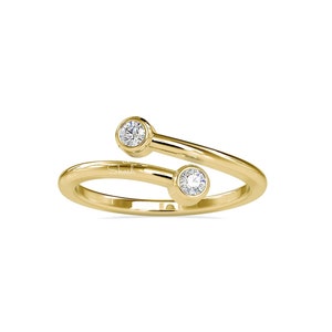 Könnte beinhalten: Ein goldener Ring mit zwei kleinen runden Diamanten, die in die Band eingefasst sind. Der Ring ist so konzipiert, dass er am Knöchel des Fingers getragen werden kann.