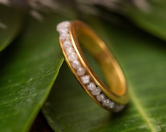 Può includere: Un anello a fascia d'oro con una fila di piccoli diamanti bianchi incastonati nella fascia.