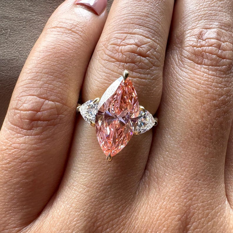 Pink marquise lab grown diamond engagement ring with heart-shaped side stones, three-stone design, 4.00 carat center diamond, elegant wedding jewelry.