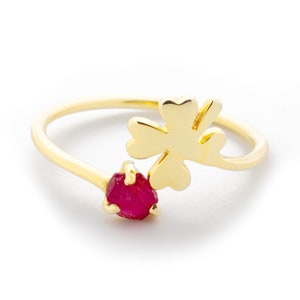 Könnte beinhalten: Ein goldener Ring mit einem Kleeblatt-Design und einem roten Edelstein.
