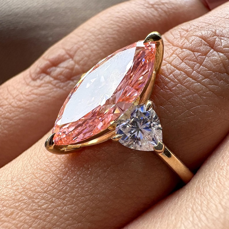 Pink marquise lab grown diamond engagement ring with heart-shaped side stones, three-stone design, 4.00 carat center diamond, elegant wedding jewelry.