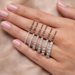 May include: A hand displays a collection of diamond eternity rings, each with a different width, ranging from 1.00 mm to 3.50 mm. The rings are set with small, sparkling diamonds. Text labels indicate the width of each ring.