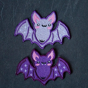 Könnte beinhalten: Zwei gestickte Bügeleisen-Aufnäher mit niedlichen Fledermäusen mit rosa Ohren und glitzernden Flügeln.