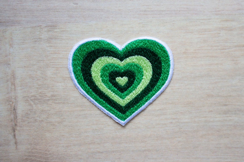 May include: A green heart-shaped patch with concentric circles of green and light green embroidery.