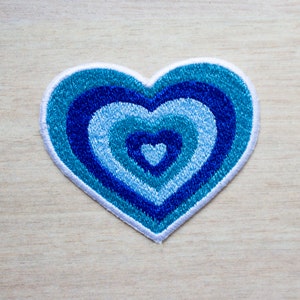 May include: A blue and white heart-shaped patch with concentric circles of blue embroidery.