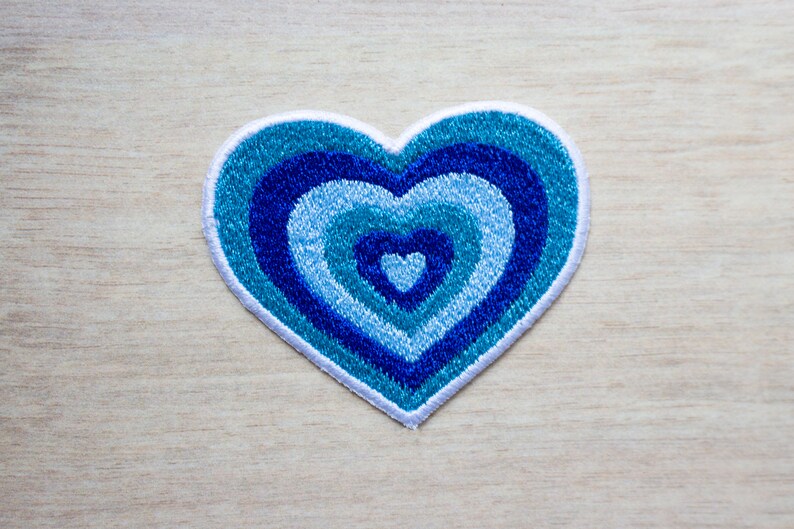 May include: A blue and white heart-shaped patch with concentric circles of blue embroidery.