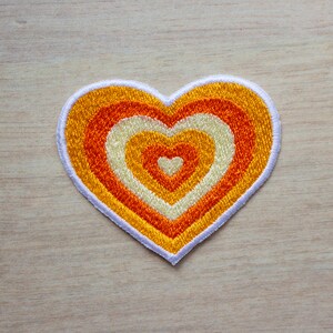 May include: A heart-shaped patch with concentric circles of orange, yellow and white embroidery.