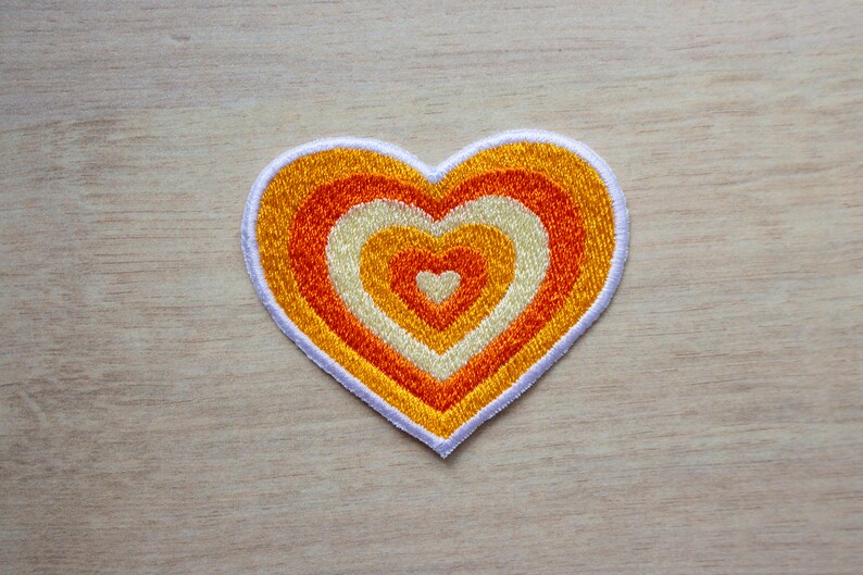 May include: A heart-shaped patch with concentric circles of orange, yellow and white embroidery.