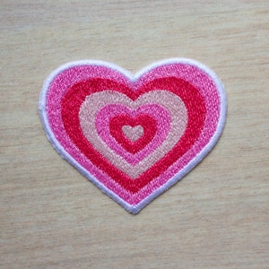 May include: A pink and white heart-shaped patch with concentric circles of pink and white embroidery.