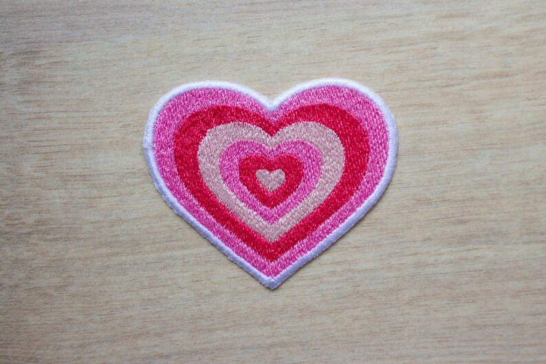 May include: A pink and white heart-shaped patch with concentric circles of pink and white embroidery.