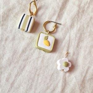 Asymmetric lemon beaded huggie hoops with green black and white stripe, flower, and lemon fruit charms, handmade polymer clay earrings
