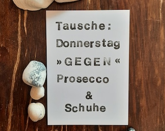 May include: A white card with black text that reads "Tausche: Donnerstag >> GEGEN << Prosecco & Schuhe". The card is sitting on a wooden surface with seashells and stones.