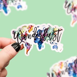 May include: A sticker with a watercolor world map design in vibrant colors, including blue, purple, yellow, and orange. The word "Wanderlust" is written in black script across the map. Additional stickers with the same design are visible in the background.