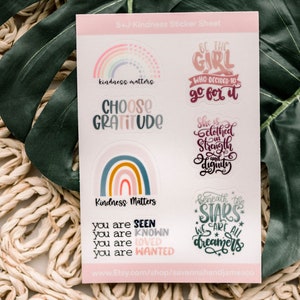 May include: A sheet of stickers with a rainbow theme. The stickers feature positive messages like "kindness matters", "choose gratitude", "be the girl who decided to go for it", "she is clothed in strength and dignity", and "beneath the stars we are all dreamers".