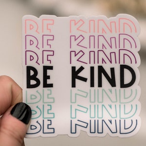 May include: A white sticker with the phrase "BE KIND" in black letters. The phrase is repeated in smaller, outlined letters in pink, purple, teal, and blue.
