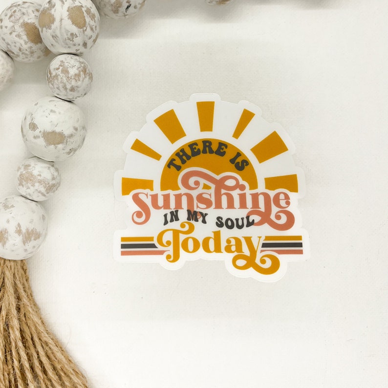 K&ouml;nnte beinhalten: Ein wei&szlig;er Aufkleber mit einer gelben Sonne und dem Text "There is Sunshine in my soul Today" in einer Retro-Schrift.