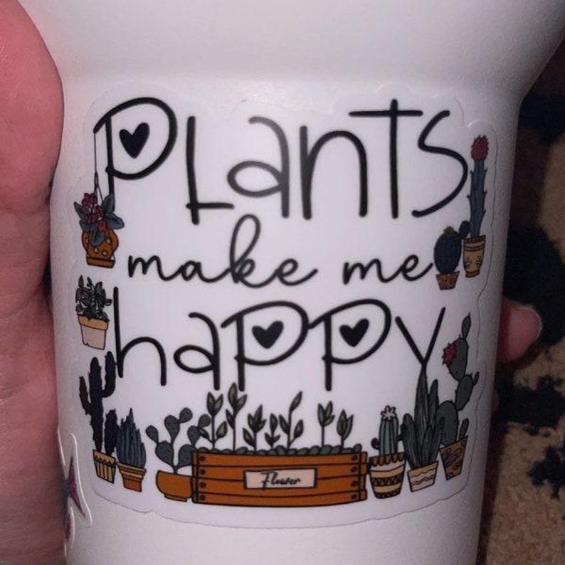 May include: A white sticker with black text that reads "Plants make me happy" with two small hearts. The sticker features a variety of potted plants, including cacti, succulents, and ferns.