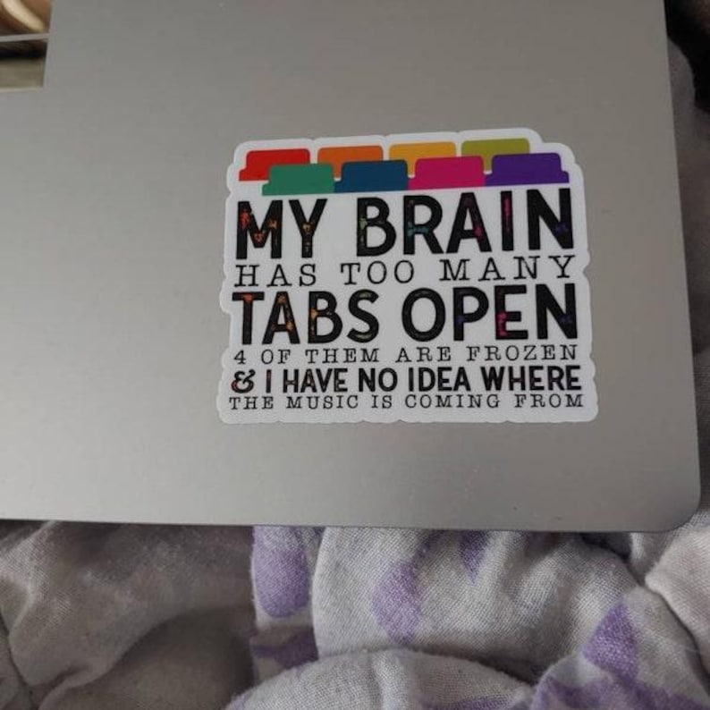 May include: A white sticker with a colorful row of tabs at the top. The sticker says "MY BRAIN HAS TOO MANY TABS OPEN 4 OF THEM ARE FROZEN & I HAVE NO IDEA WHERE THE MUSIC IS COMING FROM".