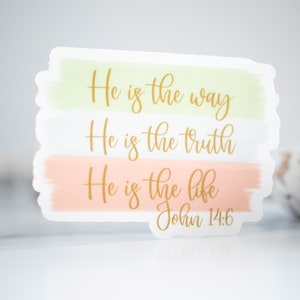 Pode incluir: Um adesivo com fundo de aquarela em tons de verde e rosa. O adesivo apresenta o texto "He is the way, He is the truth, He is the life, John 14:6" em letras douradas.