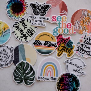 May include: Assortment of colorful stickers with positive messages and designs, including a sunflower, butterfly, rainbow, and a monstera leaf. The stickers feature phrases like "You are enough", "Be Kind", "See the good", and "Live life in full bloom".