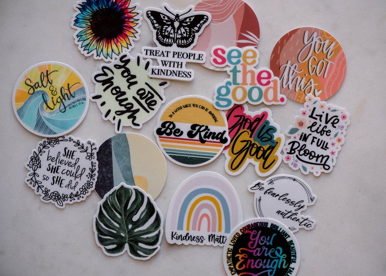 May include: Assortment of colorful stickers with positive messages and designs, including a sunflower, butterfly, rainbow, and a monstera leaf. The stickers feature phrases like "You are enough", "Be Kind", "See the good", and "Live life in full bloom".