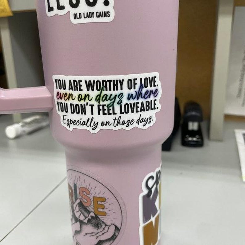 May include: A pink tumbler with a sticker that reads "You are worthy of love. even on days where you don't feel loveable. Especially on those days."