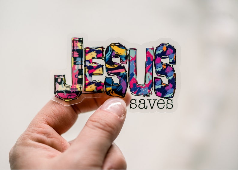 May include: A clear sticker with the word "JESUS" in colorful, abstract lettering and the word "saves" in black lettering below.