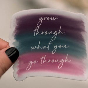 May include: A sticker with a watercolor background in shades of purple, teal, and pink. The text "grow through what you go through" is written in white cursive font.