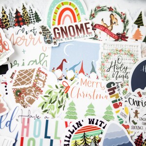 K&ouml;nnte beinhalten: Eine Auswahl an weihnachtlichen Aufklebern mit verschiedenen Designs, darunter ein Lebkuchenhaus, ein Gnom, ein Rentier und ein Weihnachtsbaum. Die Aufkleber sind auf wei&szlig;em Papier mit bunten Designs und Text gedruckt.