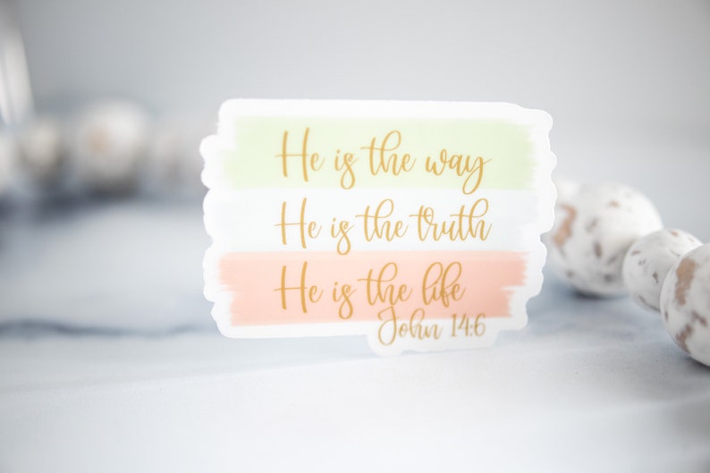 Pode incluir: Um adesivo branco com letras douradas que diz "Ele &eacute; o caminho, Ele &eacute; a verdade, Ele &eacute; a vida, Jo&atilde;o 14:6". O adesivo tem um fundo de aquarela com cores verde claro, branco e p&ecirc;ssego.