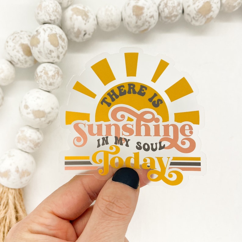 K&ouml;nnte beinhalten: Ein transparenter Aufkleber mit einer gelben Sonne und dem Text "There is sunshine in my soul today" in rosa und braunen Buchstaben.