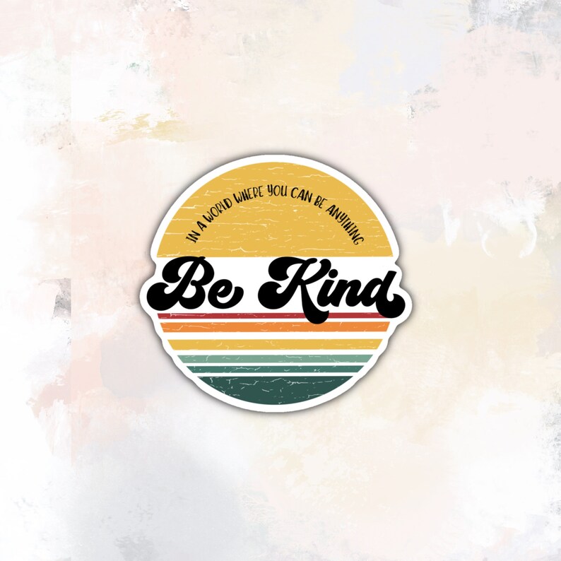 May include: A yellow and orange retro-style sticker with a distressed look. The sticker has a white border and says "In a world where you can be anything, Be Kind".
