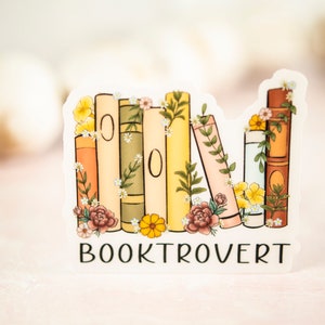 Pu&ograve; includere: Un adesivo con una pila di libri con accenti floreali e il testo "BOOKTROVERT" stampato sotto.