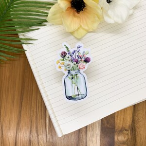 May include: A watercolor illustration of a mason jar filled with a bouquet of colorful wildflowers. The flowers are in shades of pink, purple, yellow, and white.