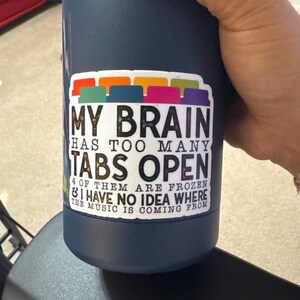 May include: A blue reusable water bottle with a sticker that says "My brain has too many tabs open & I have no idea where the music is coming from".