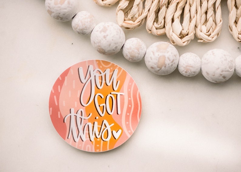 May include: A round sticker with a peach, orange, and yellow abstract design. The sticker has white text that reads 'You got this' with a small heart symbol.