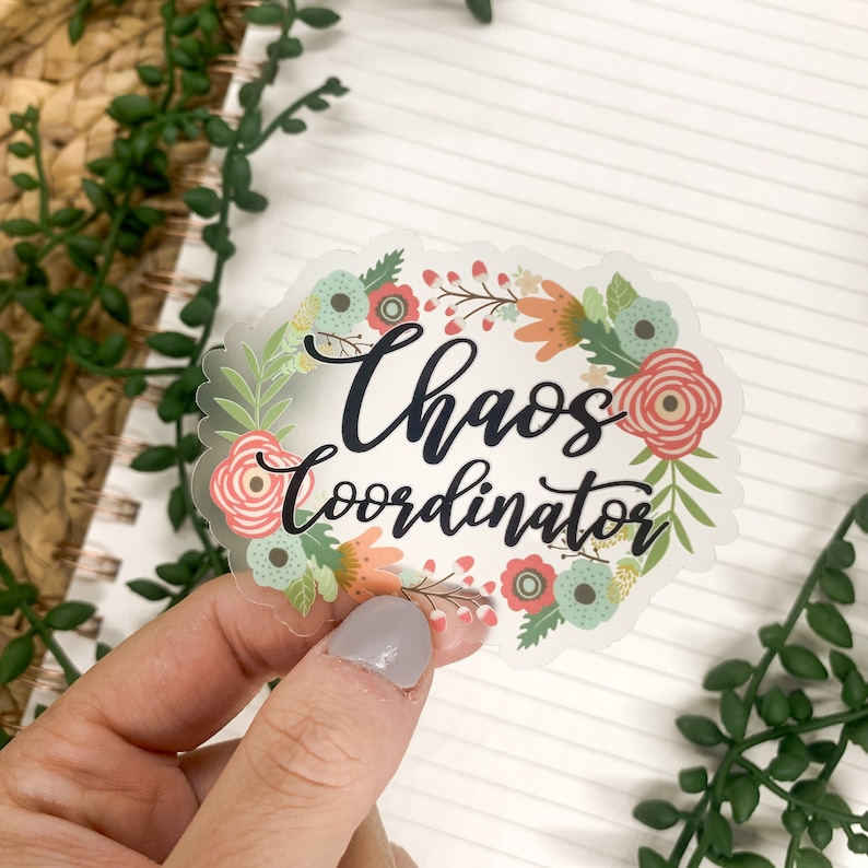 May include: A clear sticker with a floral wreath design. The text "Chaos Coordinator" is written in black script inside the wreath.