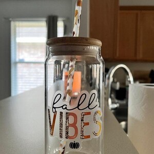 K&ouml;nnte beinhalten: Eine klare Glaswasserflasche mit Bambusdeckel und Strohhalm. Die Flasche hat einen Aufkleber mit der Aufschrift "fall vibes" mit einem K&uuml;rbis- und Leopardenmuster.