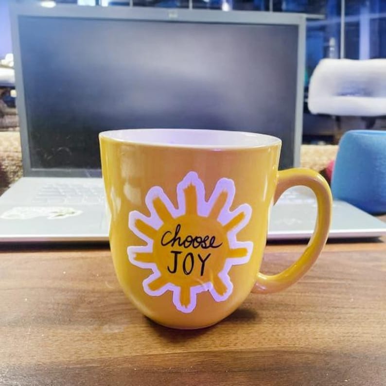 May include: Yellow ceramic mug with a white sun design and the text "choose JOY" in black lettering.