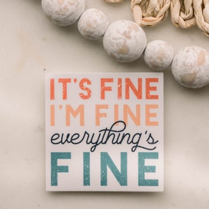 Peut inclure: Un panneau carr&eacute; blanc avec le texte "It's fine I'm fine everything's fine" dans une police color&eacute;e et superpos&eacute;e.