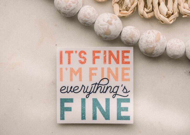 Peut inclure: Un panneau carr&eacute; blanc avec le texte "It's fine I'm fine everything's fine" dans une police color&eacute;e et superpos&eacute;e.