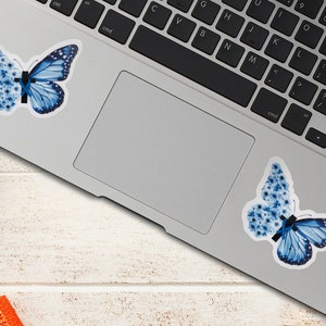 May include: Two blue butterfly stickers on a silver laptop. The butterflies are made of blue flowers and have a black ribbon in the center.